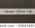 White and Grey coloured paper background with Never Give Up motivational handwritten message 69043480