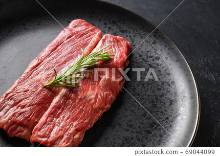 Raw marbled ribeye steak in black plate.  69044099