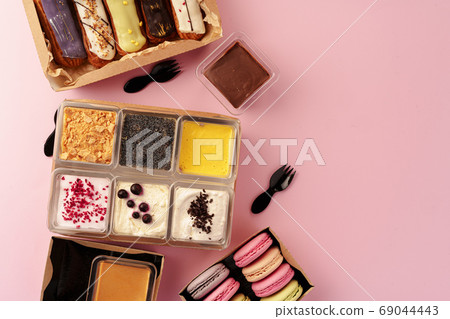 Carton boxes with eclair cakes and cookies on pink surface Carton boxes with eclair cakes and cookies on pink surface 69044443