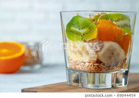 Glass with fruit pieces and oatmeal muesli on wooden board 69044454