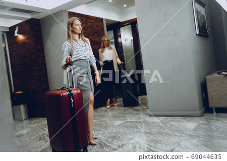 Two young women in formal clothes entering hotel lobby 69044635