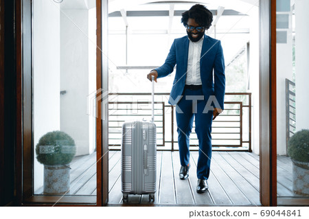 Black man in formal suit with packed suitcase entering hotel door Black man in formal suit with packed suitcase entering hotel door 69044841