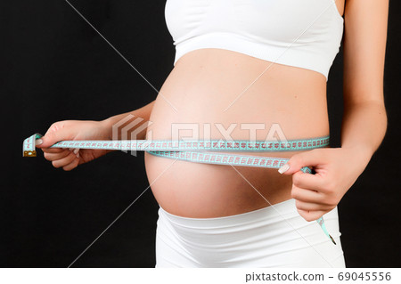 Close up image of tape measure on pregnant woman's belly at black background. Future mother is measuring her growing tummy to check baby development. Copy space Close up image of tape measure on pregnant woman's belly at black background. Future mother is measuring her growing tummy to check baby development. Copy space 69045556