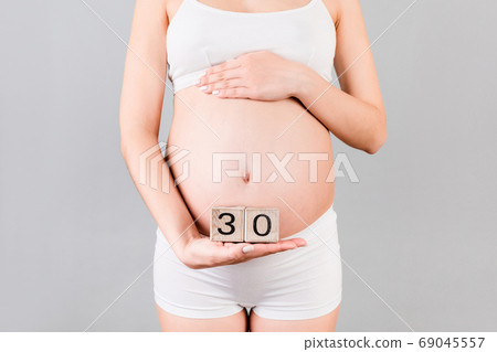 Cropped image of pregnant woman in white underwear showing thirty weeks of pregnancy cubes at gray background. Waiting for a baby. Copy space 69045557