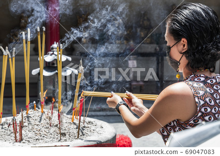 A young woman wearing face mask is burning incense in a Chinese 69047083