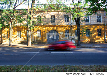 Red car driving on free street at sunset i front of yellow building, motion blur Red car driving on free street at sunset i front of yellow building, motion blur 69048587