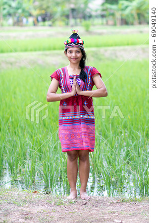 A young Asian woman in traditional dress doing traditional greeting sawasdee. A young Asian woman in traditional dress doing traditional greeting sawasdee. 69049140