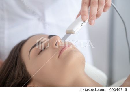 Dark-haired woman having laser skin treatment and looking relaxed Dark-haired woman having laser skin treatment and looking relaxed 69049746