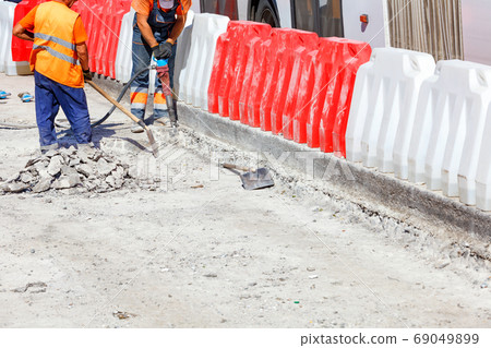 A team of workers cleans some of the concrete with a jackhammer during road construction. 69049899