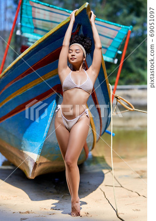 Beautiful young woman in bikini posing near to old fishing boat 69051097