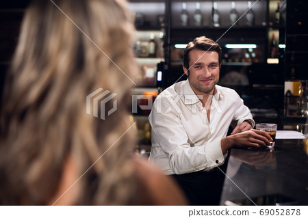 a handsome man saw a pretty young blonde girl in the bar and smiles at her 69052878