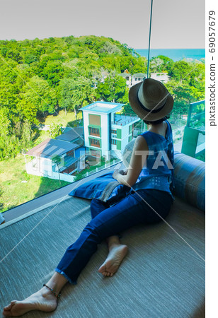 Asian woman in comfortable dress with a relaxed hat in the room looking nature outside Asian woman in comfortable dress with a relaxed hat in the room looking nature outside 69057679