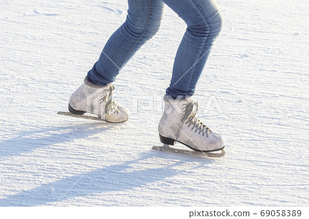 legs of a girl in blue jeans and white skates on an ice rink. ho 69058389