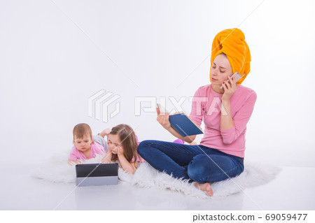 woman with book in her hands is talking on phone. Children watch cartoon on their tablet. mom washed her hair. towel on head. Hobbies and recreation with gadgets. woman with book in her hands is talking on phone. Children watch cartoon on their tablet. mom washed her hair. towel on head. Hobbies and recreation with gadgets. 69059477