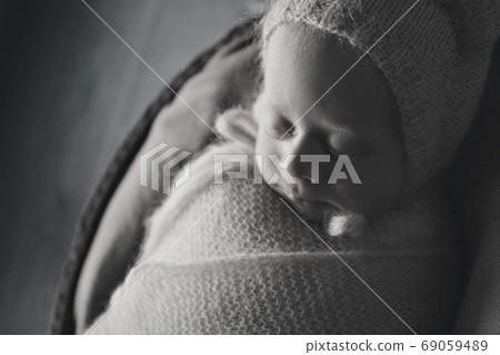 a small child in a basket sleeps in a warm knitted hat with a pompom 69059489