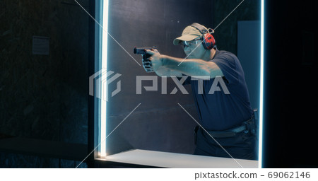 Mature shooter firing pistol in dark range Mature shooter firing pistol in dark range 69062146