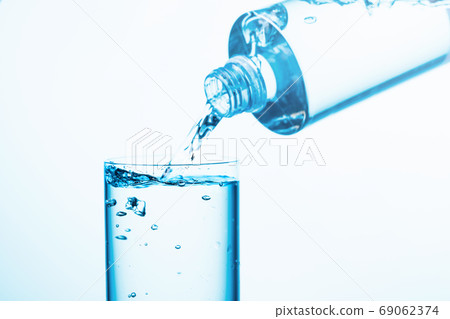 Pouring water from a bottle into glass on a blue background. 69062374