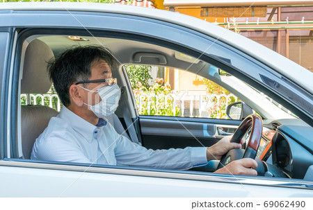 Middle-aged man wearing a mask is driving a car Middle-aged man wearing a mask is driving a car 69062490