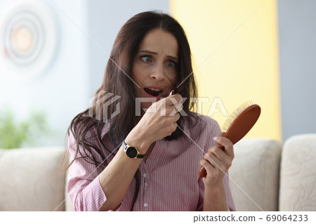 Frightened woman holds comb in her hands and looks at her hai 69064233