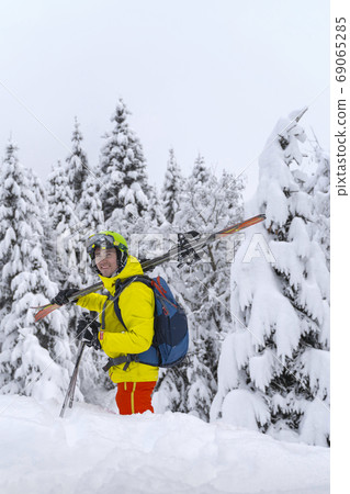 Man in yellow with blue backpack skiing stay with many firs around and soft powdery snow. Man in yellow with blue backpack skiing stay with many firs around and soft powdery snow. 69065285