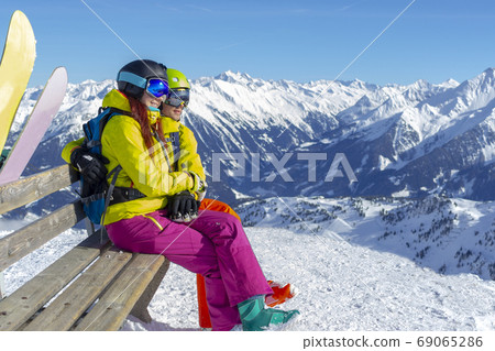 Happy young couple sitting on a bench with snowboards a snowy slope and looking at Alps. Happy young couple sitting on a bench with snowboards a snowy slope and looking at Alps. 69065286