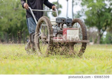 Worker mowing grass with machine in the public garden Worker mowing grass with machine in the public garden 69065309
