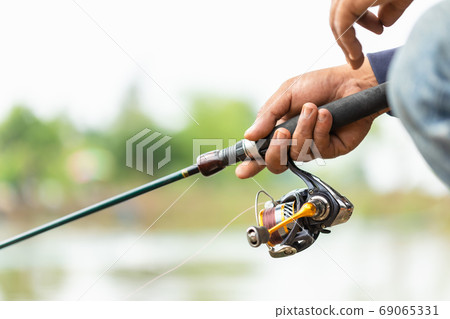 Fishing reel and rod in fisherman hand in a pond 69065331