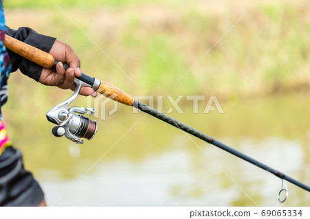 Fishing reel and rod in fisherman hand in a pond 69065334