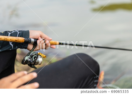 Fishing reel and rod in fisherman hand in a pond Fishing reel and rod in fisherman hand in a pond 69065335