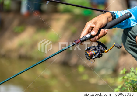 Fishing reel and rod in fisherman hand in a pond Fishing reel and rod in fisherman hand in a pond 69065336