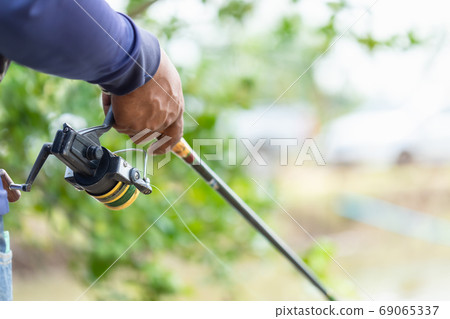 Fishing reel and rod in fisherman hand in a pond Fishing reel and rod in fisherman hand in a pond 69065337