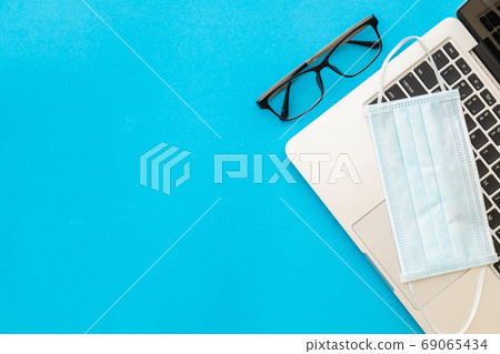 New preventive mask on laptop and eye glasses on blue background New preventive mask on laptop and eye glasses on blue background 69065434
