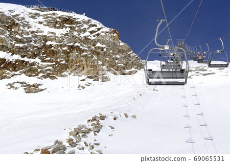Chair lift move up and cableway in the foreground against the background mountains and blue sky Chair lift move up and cableway in the foreground against the background mountains and blue sky 69065531