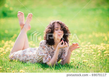 Young attractive woman with curly long hair posing in spring blooming garden, apple trees 69070117