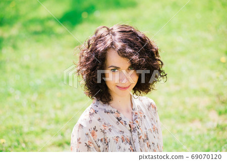 Young attractive woman with curly long hair posing in spring blooming garden, apple trees Young attractive woman with curly long hair posing in spring blooming garden, apple trees 69070120