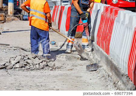 A team of workers cleans some of the concrete with a jackhammer and shovels during road repairs. 69077394