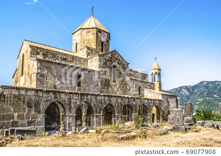 South side of the Odzun monastery with a view of the arched gallery with a bell tower and stone crosses against the background of wooded mountains South side of the Odzun monastery with a view of the arched gallery with a bell tower and stone crosses against the background of wooded mountains 69077908