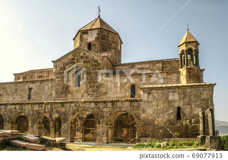 Monastery Odzun with an arched gallery and bell tower, basalt crosses on the south side at sunset Monastery Odzun with an arched gallery and bell tower, basalt crosses on the south side at sunset 69077913