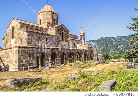 South side of the Odzun monastery at sunset, with a view of the arched gallery with a bell tower against the background of wooded mountains South side of the Odzun monastery at sunset, with a view of the arched gallery with a bell tower against the background of wooded mountains 69077915