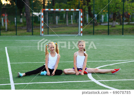 Girls sit on a twine on a sports field. 69078785