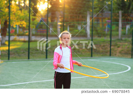 Girl in a tracksuit with a hoop in her hands on the playground 69078845