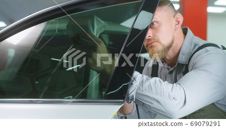 Bearded mechanic spraying tinted window 69079291