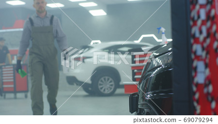 Male mechanic walking in garage and cleaning car Male mechanic walking in garage and cleaning car 69079294