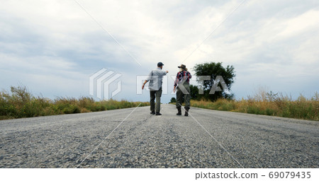 Anonymous farmers walking on road and talking Anonymous farmers walking on road and talking 69079435