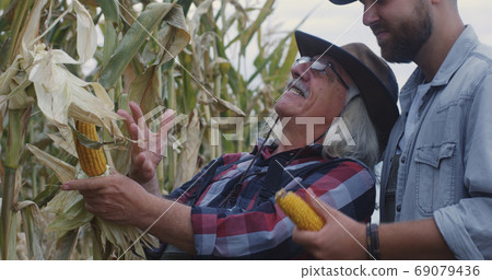 Cheerful elderly farmer showing corn to grandson 69079436