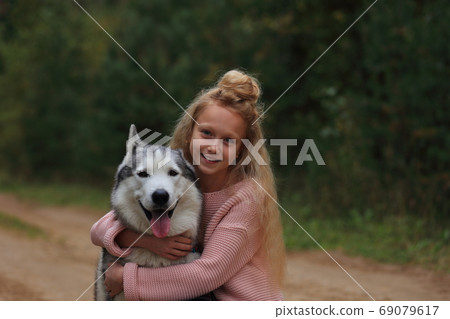 A girl with a husky walks in the forest. 69079617