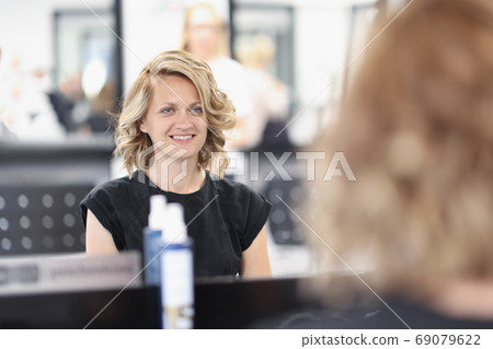 Woman with an evening hairstyle in a beauty salon sits in front of mirror and smiles Woman with an evening hairstyle in a beauty salon sits in front of mirror and smiles 69079622