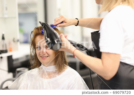 Hairdresser makes client's hair styled with hairdryer and comb. Hairdresser makes client's hair styled with hairdryer and comb. 69079720