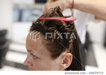 Woman with wet hair is pinning hairpins on her strands. Woman with wet hair is pinning hairpins on her strands. 69079733