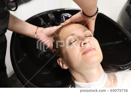 Master washes woman's head in sink in hairdresser. Master washes woman's head in sink in hairdresser. 69079736